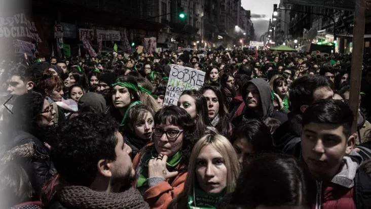 Multitud apretada de manifestantes, muchos con pañuelos verdes, en una calle de noche