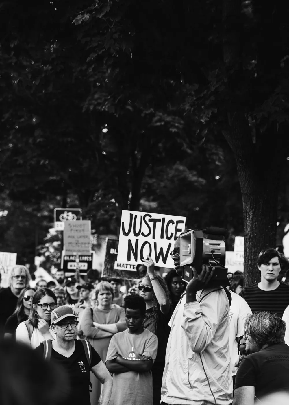 Multitud en una protesta, en blanco y negro, con un cartel «Justice now» en alto