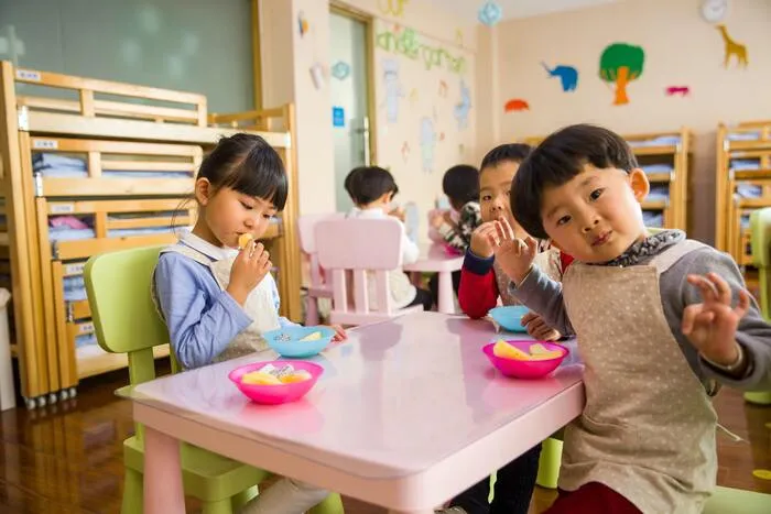 Niños sentados alrededor de una mesa rosada comen en el salón de una guardería