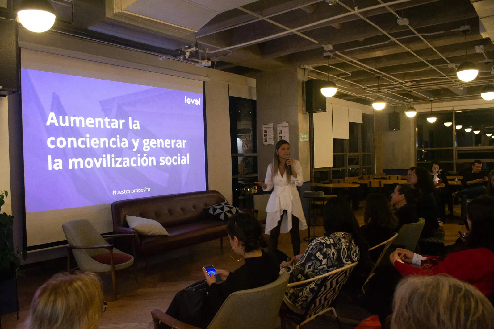 Oradora de pie junto a una pantalla con la diapositiva «Aumentar la conciencia y generar la movilización social» en el lanzamiento de Revista Level