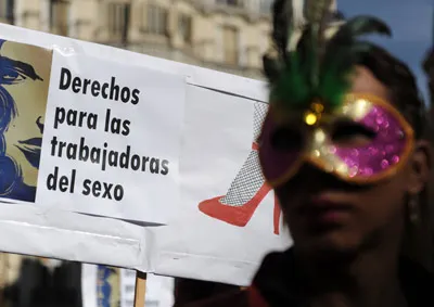 Manifestante con antifaz de carnaval junto a una pancarta que dice «Derechos para las trabajadoras del sexo»