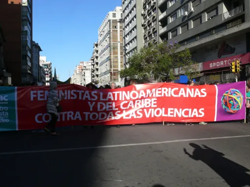 Pancarta roja «Feministas latinoamericanas y del Caribe contra todas las violencias» extendida en una avenida