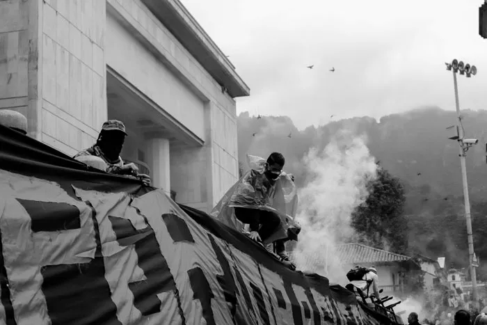 Pancarta grande y humo frente a un edificio durante una protesta, en blanco y negro