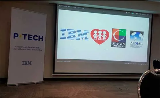 Salón con una pantalla que muestra los logos de IBM, Fe y Alegría, Magis Américas y Aunal, junto a un cartel de P-TECH