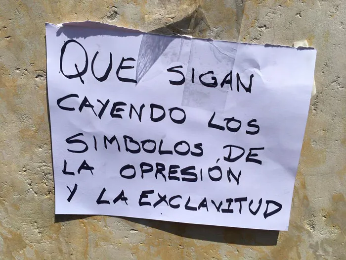 Papel pegado en un muro con el mensaje «Que sigan cayendo los símbolos de la opresión y la esclavitud»