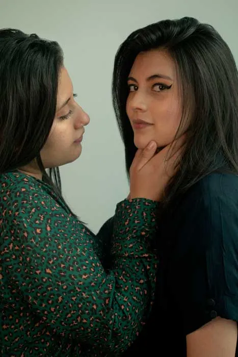 Dos mujeres posan cerca una de la otra, una con la mano en el rostro de la otra