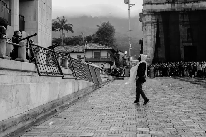 Persona de blanco camina sola por una calle empedrada junto a un edificio en blanco y negro