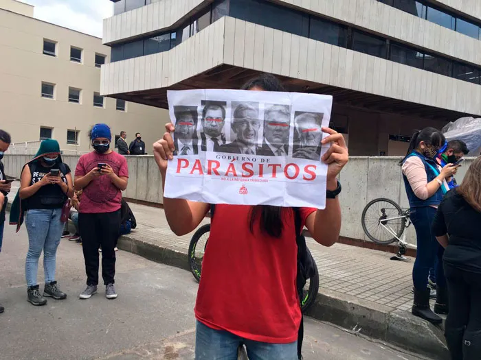Persona sostiene un cartel con cuatro rostros y la palabra «Parásitos» durante el Paro Nacional