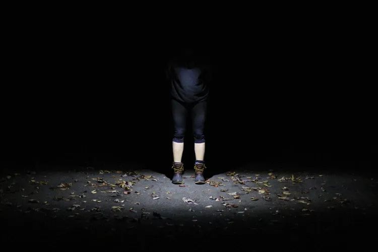 Piernas de una persona de pie en la oscuridad, iluminadas por un haz de luz sobre el suelo