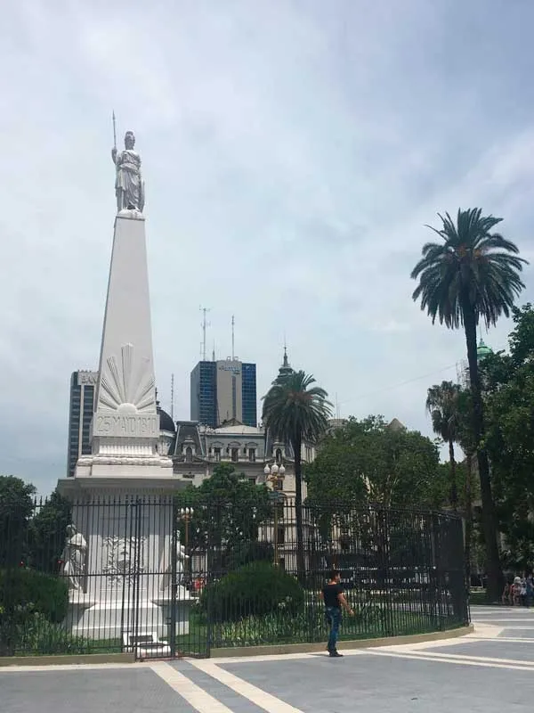 Pirámide de Mayo con la estatua en lo alto, rodeada de palmeras, en la Plaza de Mayo de Buenos Aires