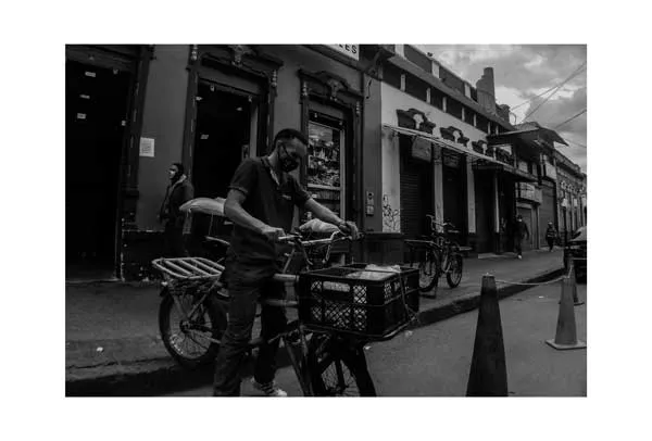 Repartidor con una bicicleta de carga con cajas en una calle del centro, en blanco y negro
