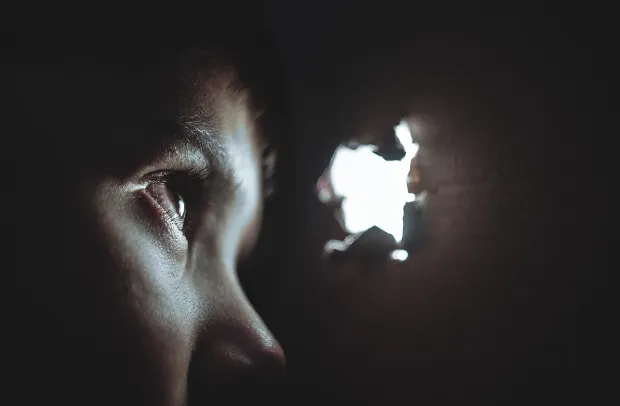Primer plano del rostro de perfil de una persona que mira por un agujero de luz en la oscuridad