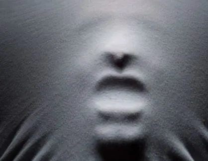 Rostro que se presiona contra una tela gris tensada, con la boca y la nariz marcadas en relieve