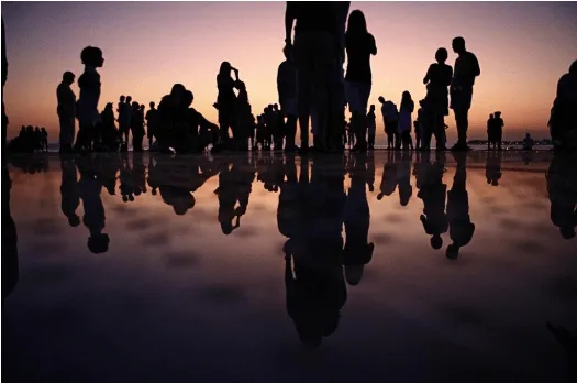 Siluetas de personas en la orilla de un lago al atardecer con su reflejo en el agua