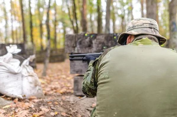 Soldado con sombrero de camuflaje apunta un fusil desde una trinchera con sacos de arena en un bosque