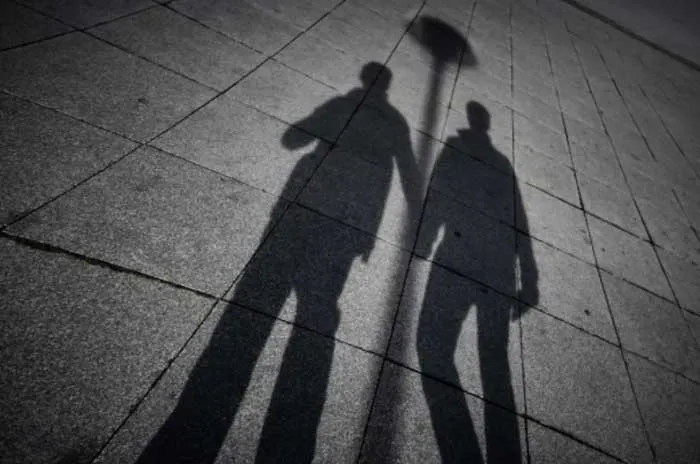 Sombras de dos personas de pie proyectadas sobre un pavimento de baldosas