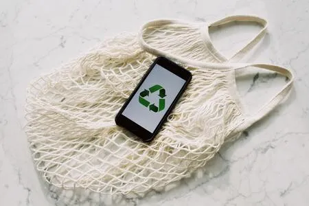 Teléfono con el símbolo de reciclaje sobre una bolsa de red blanca en una mesa de mármol