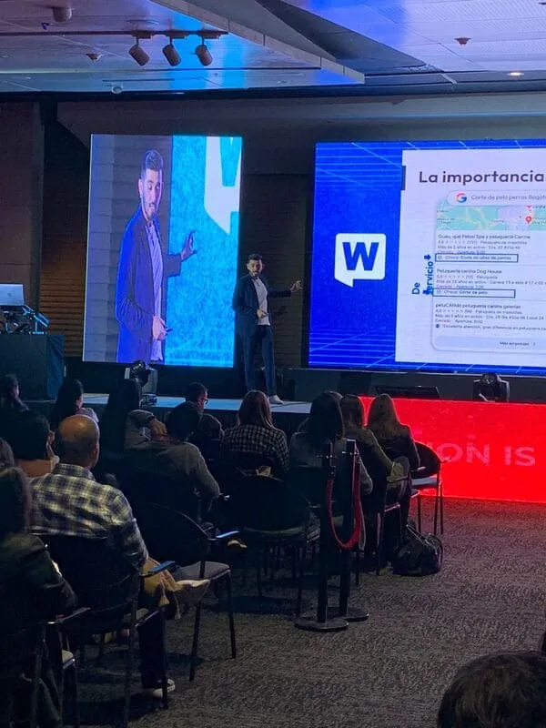 Público sentado ante un orador en el escenario del WebCongress Multiverse, con pantallas que muestran una diapositiva