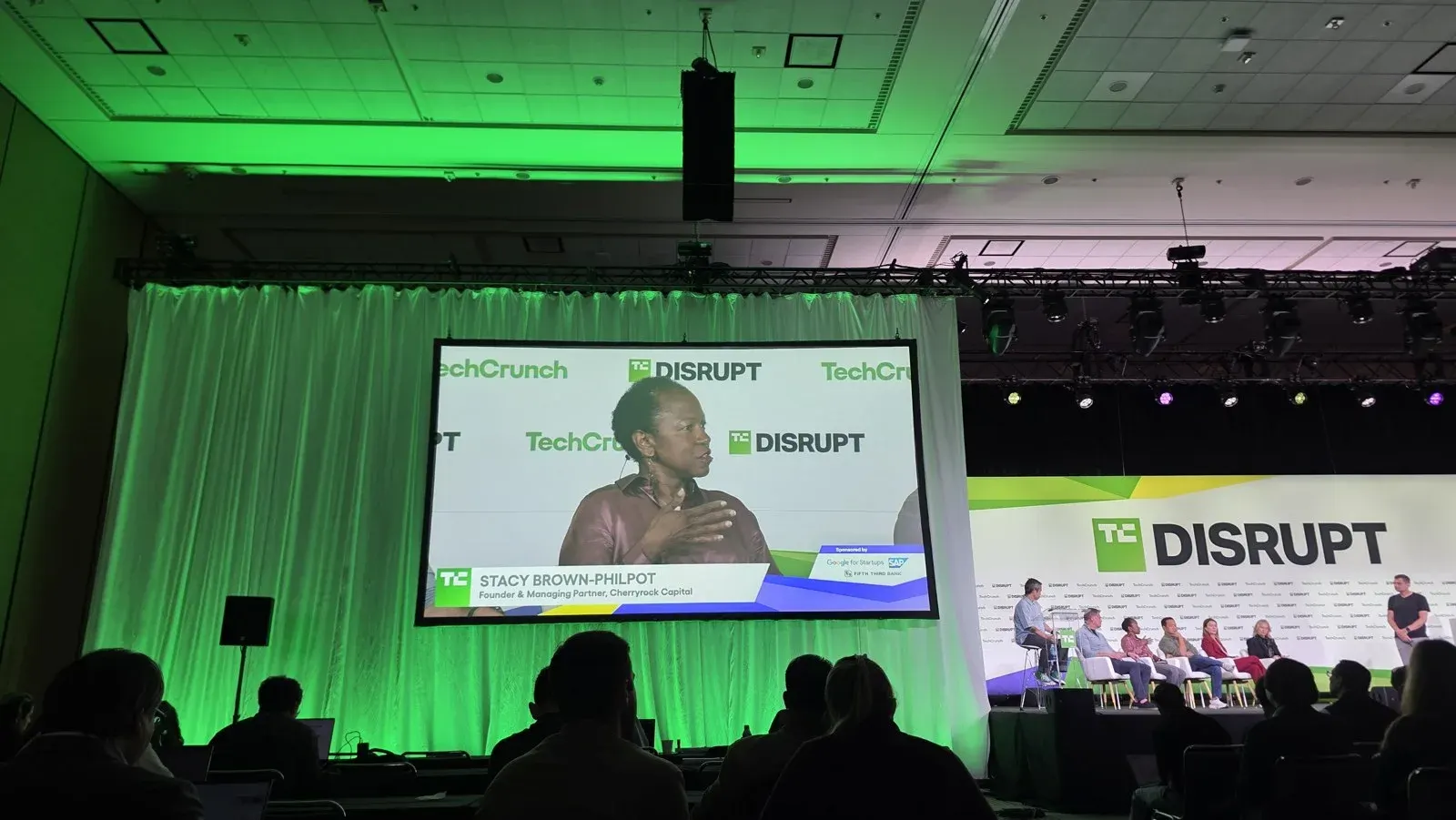 Stacy Brown-Philpot, jurado de la final del Startup Battlefield, en la pantalla del escenario de TechCrunch Disrupt 2026, con el panel de jurados al fondo